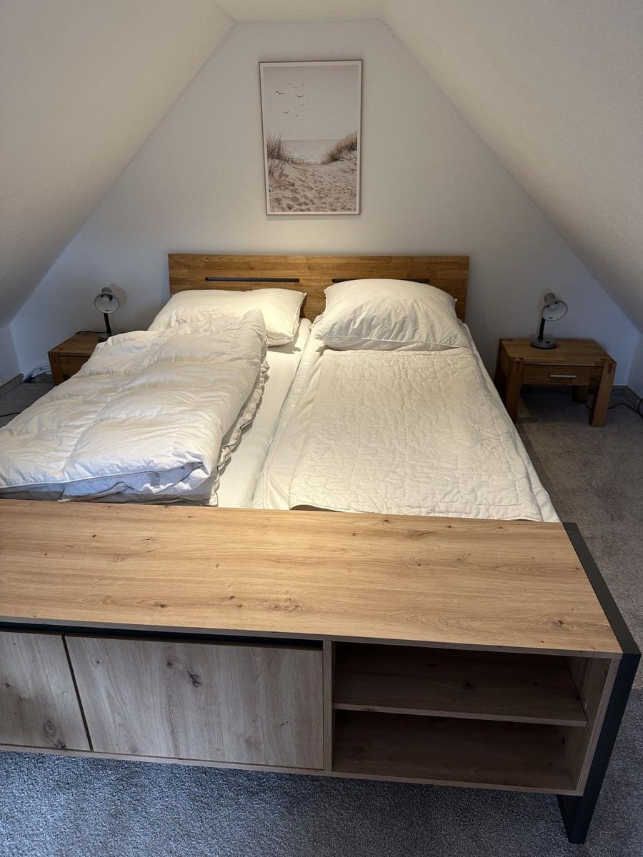 Schlafzimmer mit Doppelbett, Holzkommode und Wandbild an schrägen Wänden.