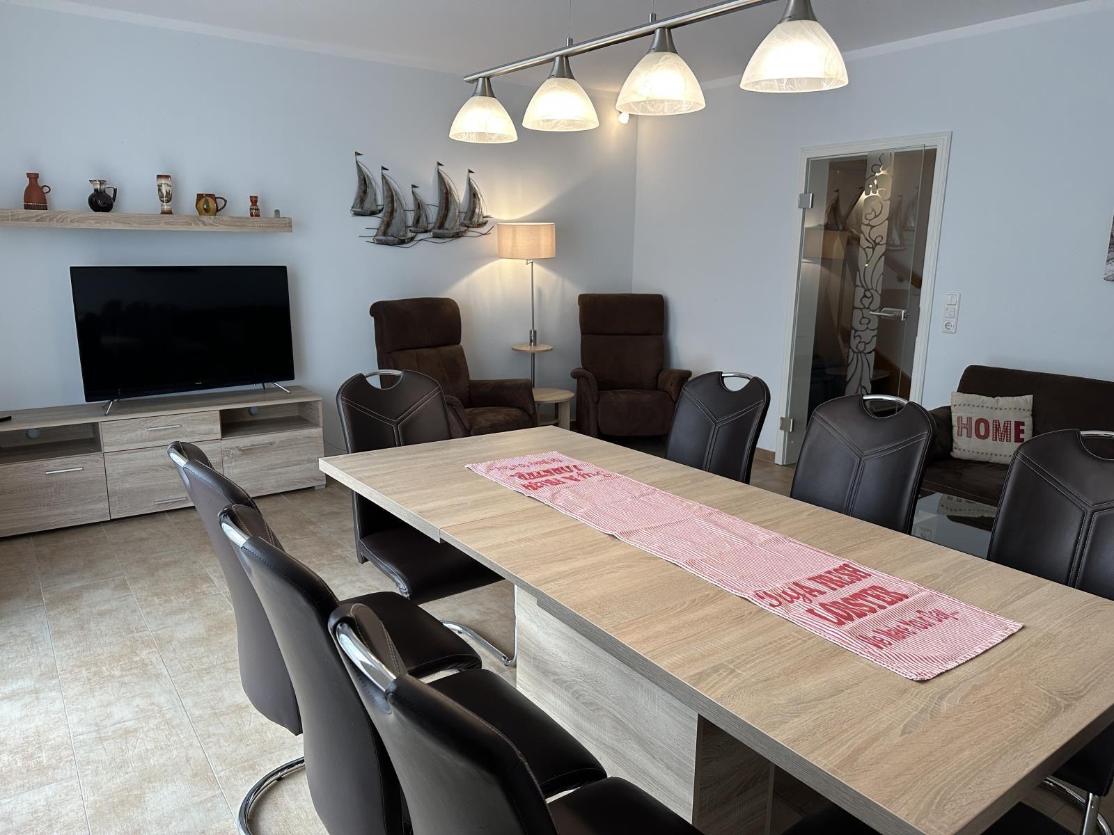 Esszimmer mit Esstisch, Stühlen und Fernseher. Wanddekoration und Beleuchtung.