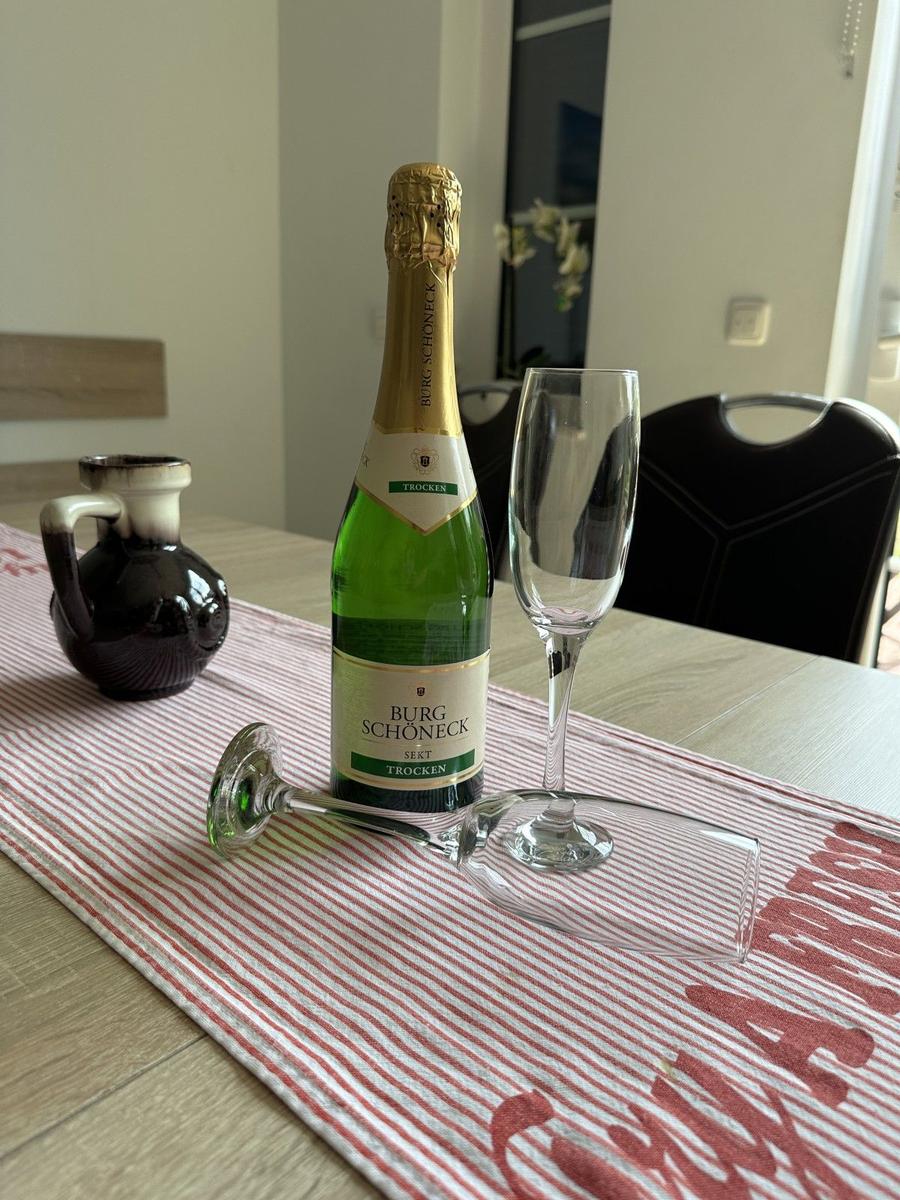 Auf dem Tisch steht eine Flasche Sekt und zwei Gläser auf einem Tischläufer.