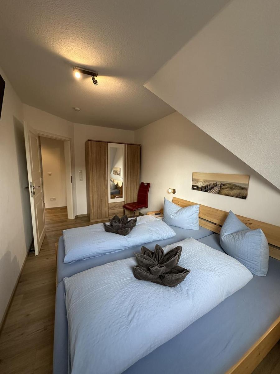 Doppelbett mit blauen Bettwäsche und Holzrahmen. Wandbild, Kleiderschrank und roter Stuhl.