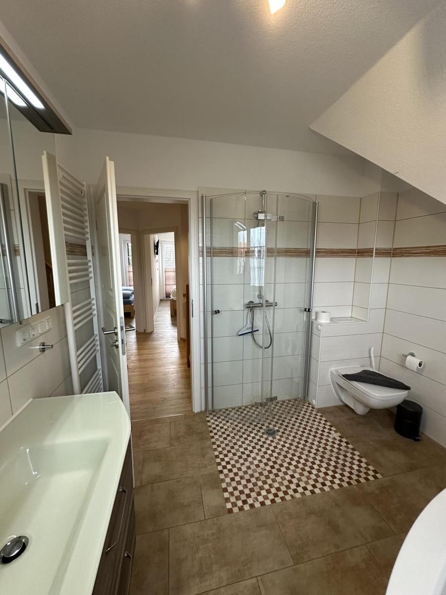 Badezimmer mit Dusche, WC und Waschbecken. Fliesenboden und Spiegel.