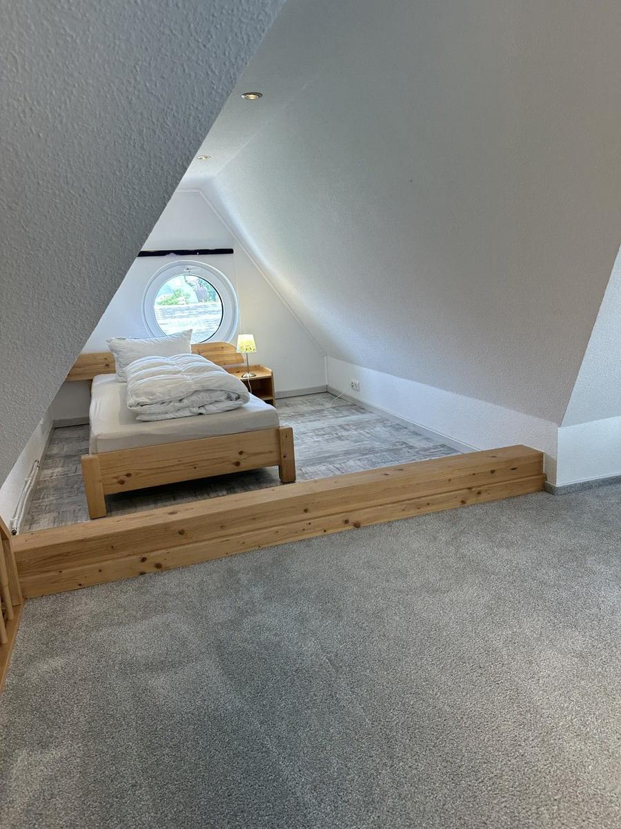 Schlafzimmer mit Holzbett und runden Fenster unter Dachschräge