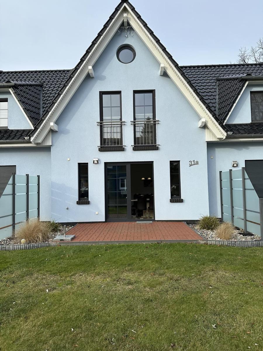 Moderne Villa mit Terrasse und grünem Garten. Eingangstür und Fenster sind schwarz.