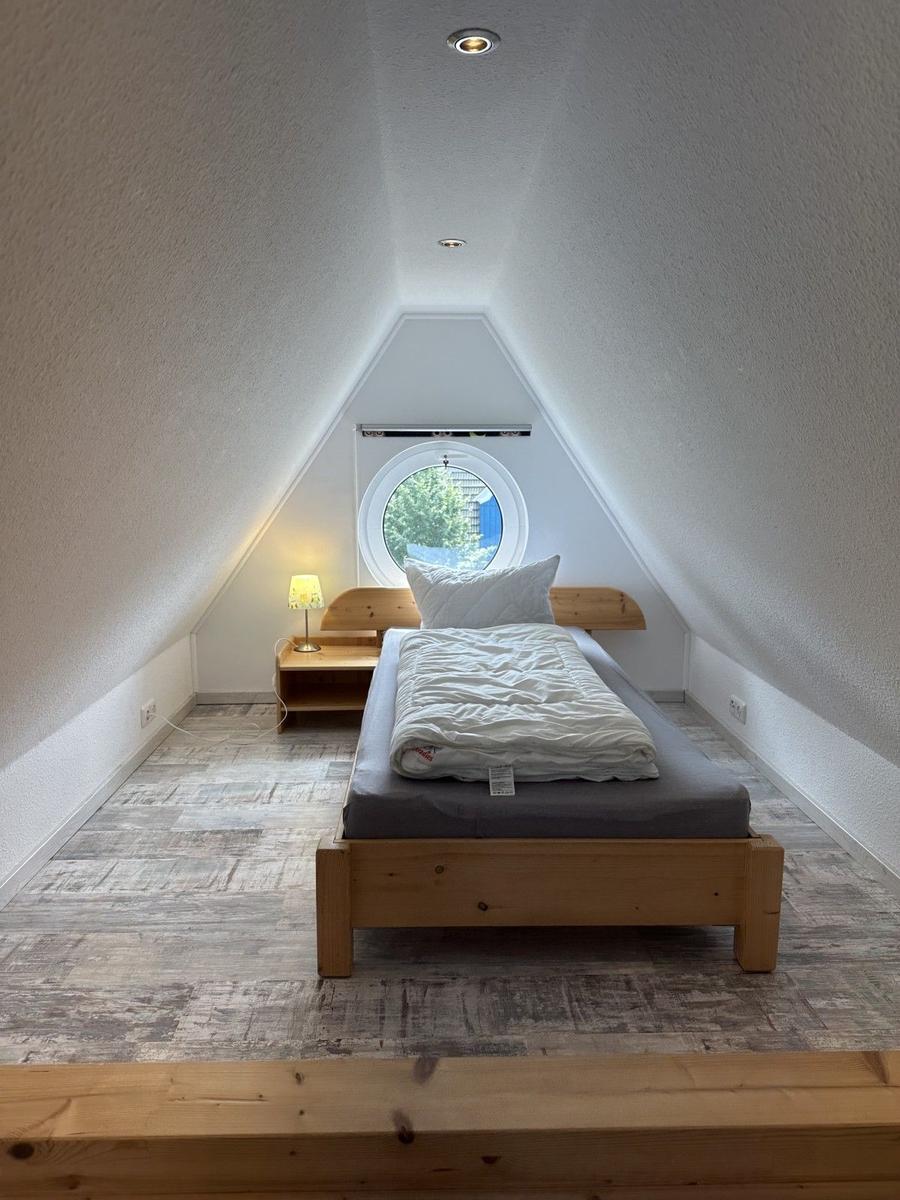 Schlafzimmer mit Holzbett, runder Fenster und Holzfußboden.