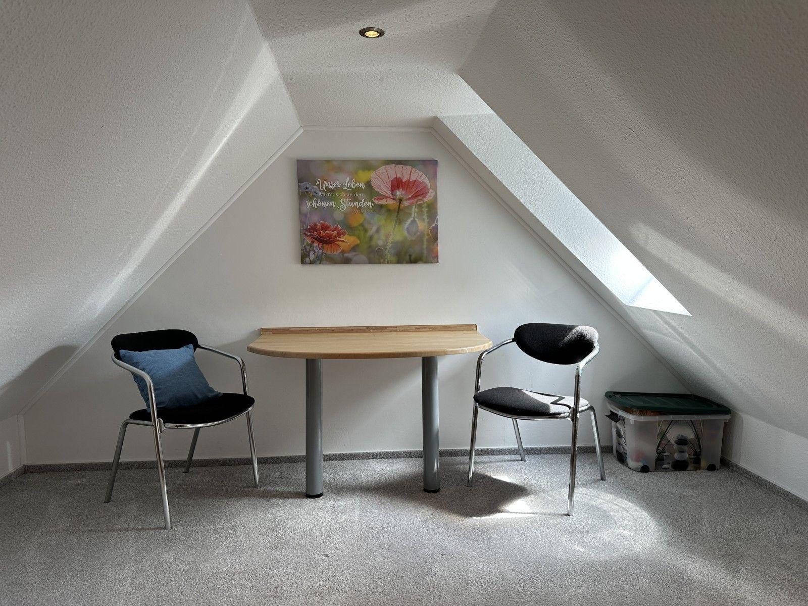 Dachgeschosszimmer mit Tisch, zwei Stühlen und Wandbild