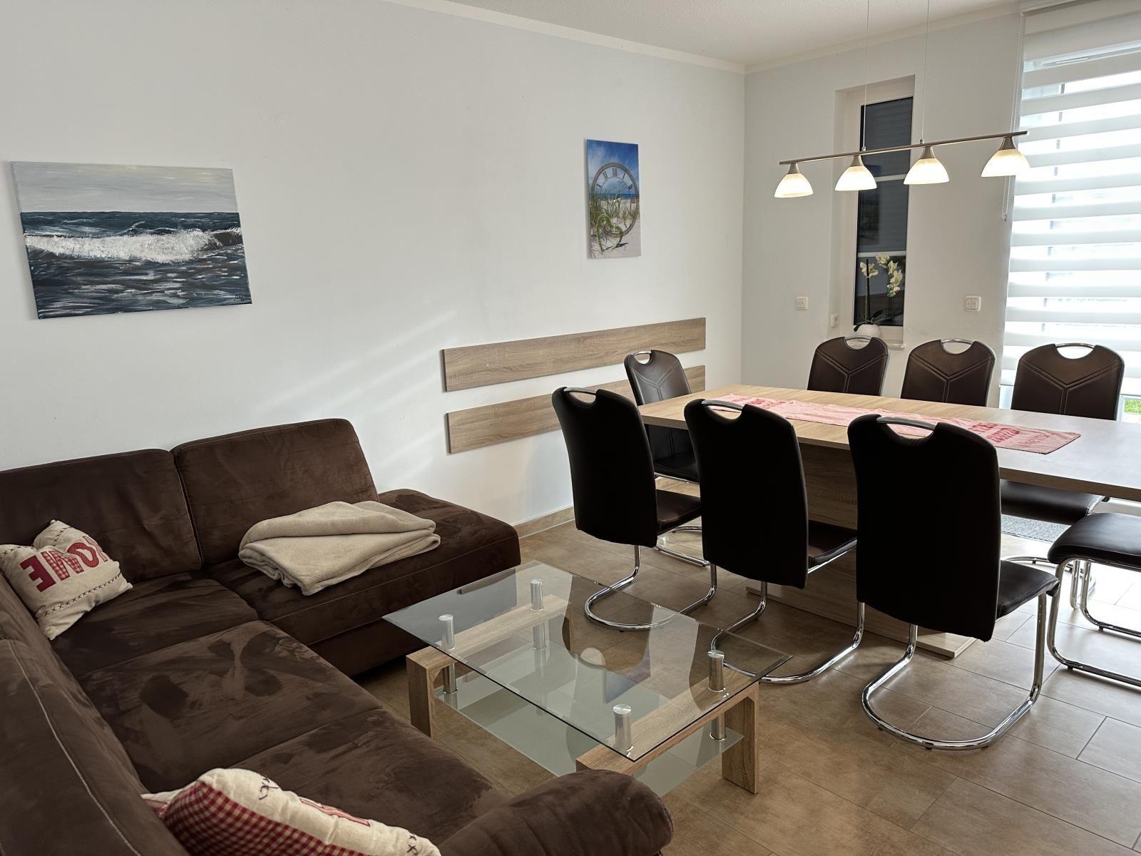 Wohn- und Essbereich mit Sofa, Tisch und Stühlen sowie Wandbildern.