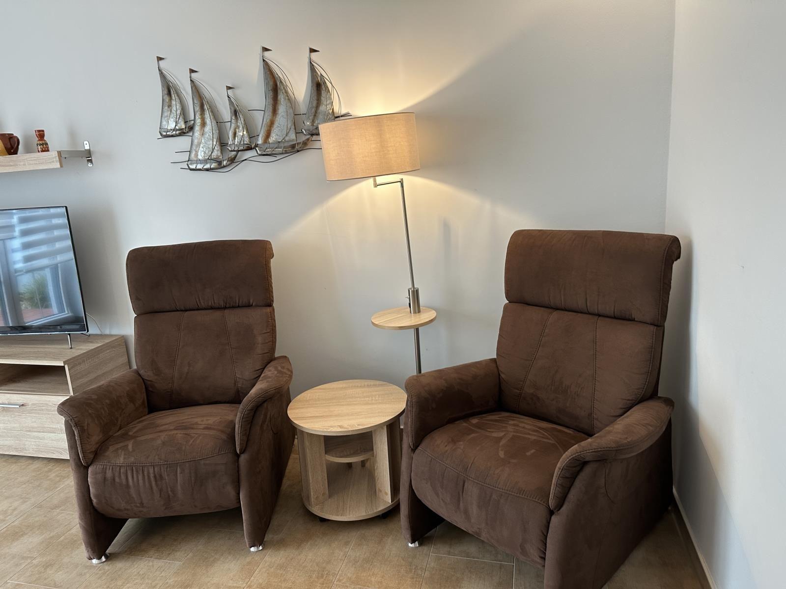 Zwei braune Sessel, Tisch und Stehlampe im Wohnbereich.