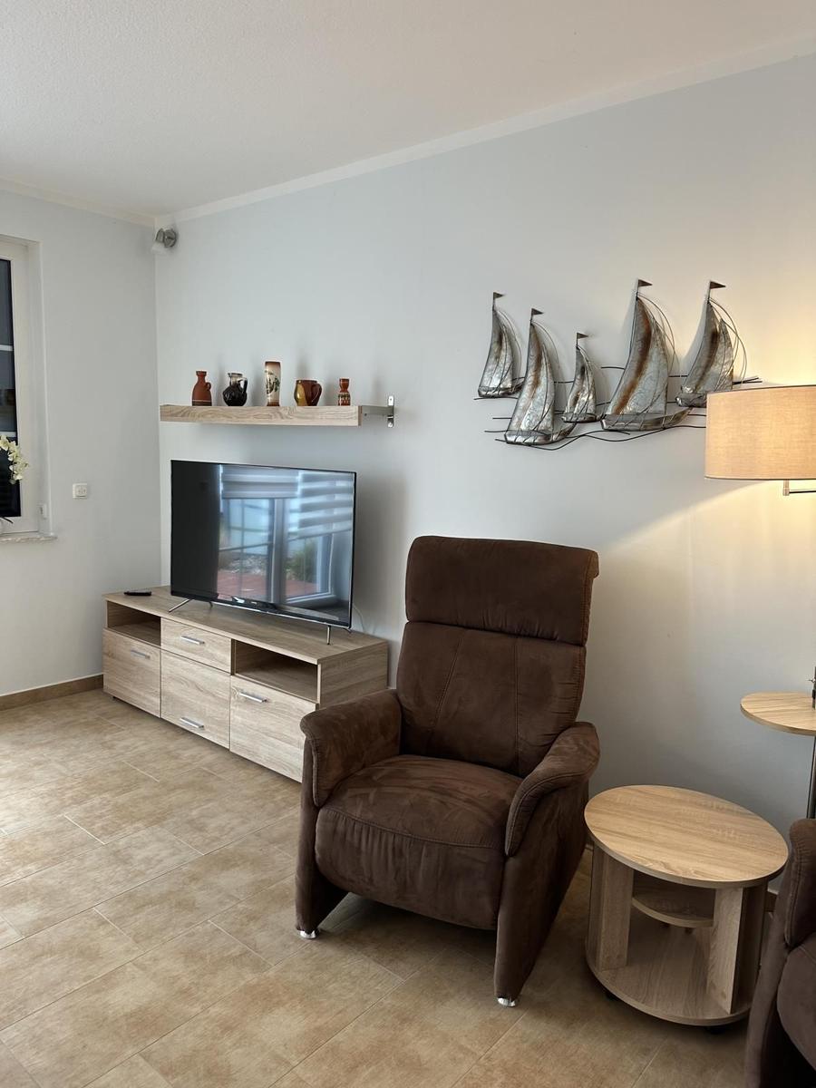 Wohnzimmer mit braunem Sessel, Fernseher und Wanddekoration mit Schiffen.