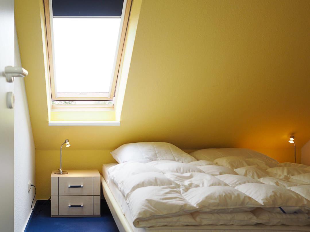 Schlafzimmer mit Dachschräge, Fenster und Bett mit weißer Bettwäsche.