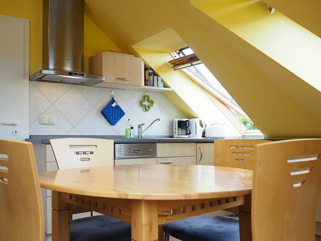 Küche mit Essbereich unter Dachschrägen, Holztisch und -stühle, Fenster und Küchengeräte.