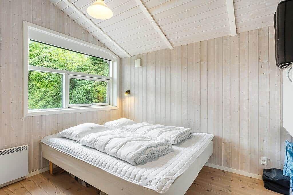Bedroom with wooden walls, bed, and window to the forest.