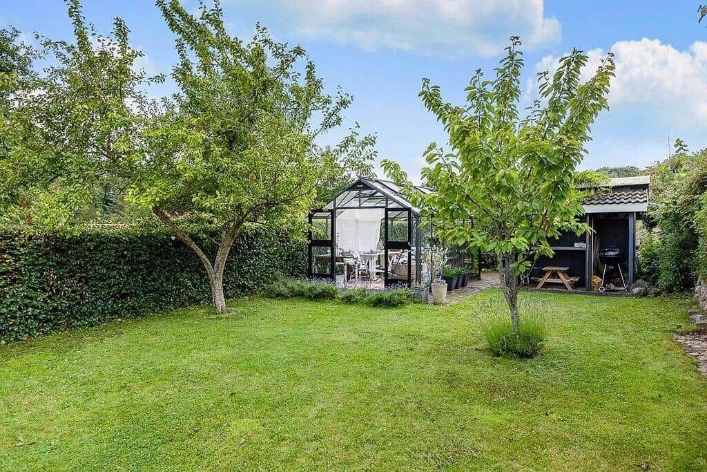 Garden with glasshouse, grill shed, and trees under blue sky.