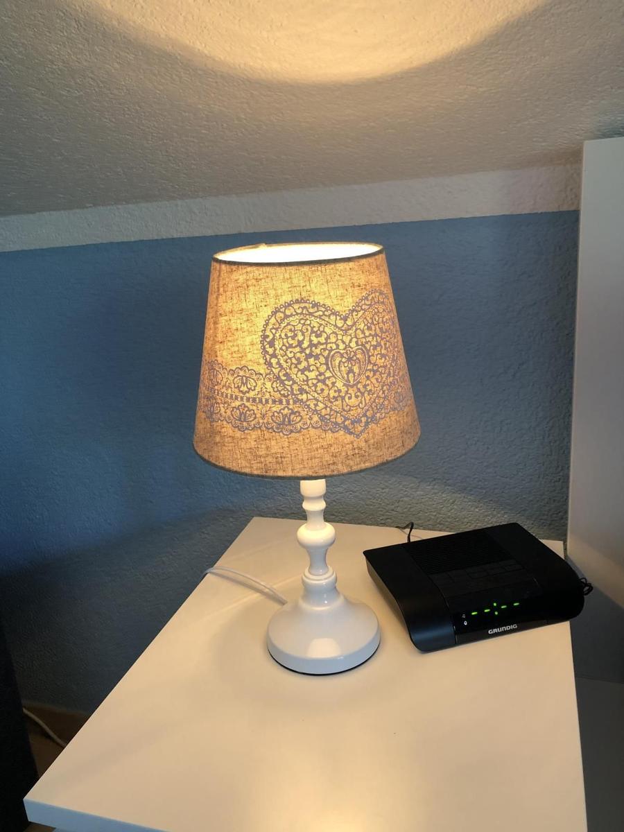 Tischlampe mit Herz-Muster und Router auf weißem Tisch.