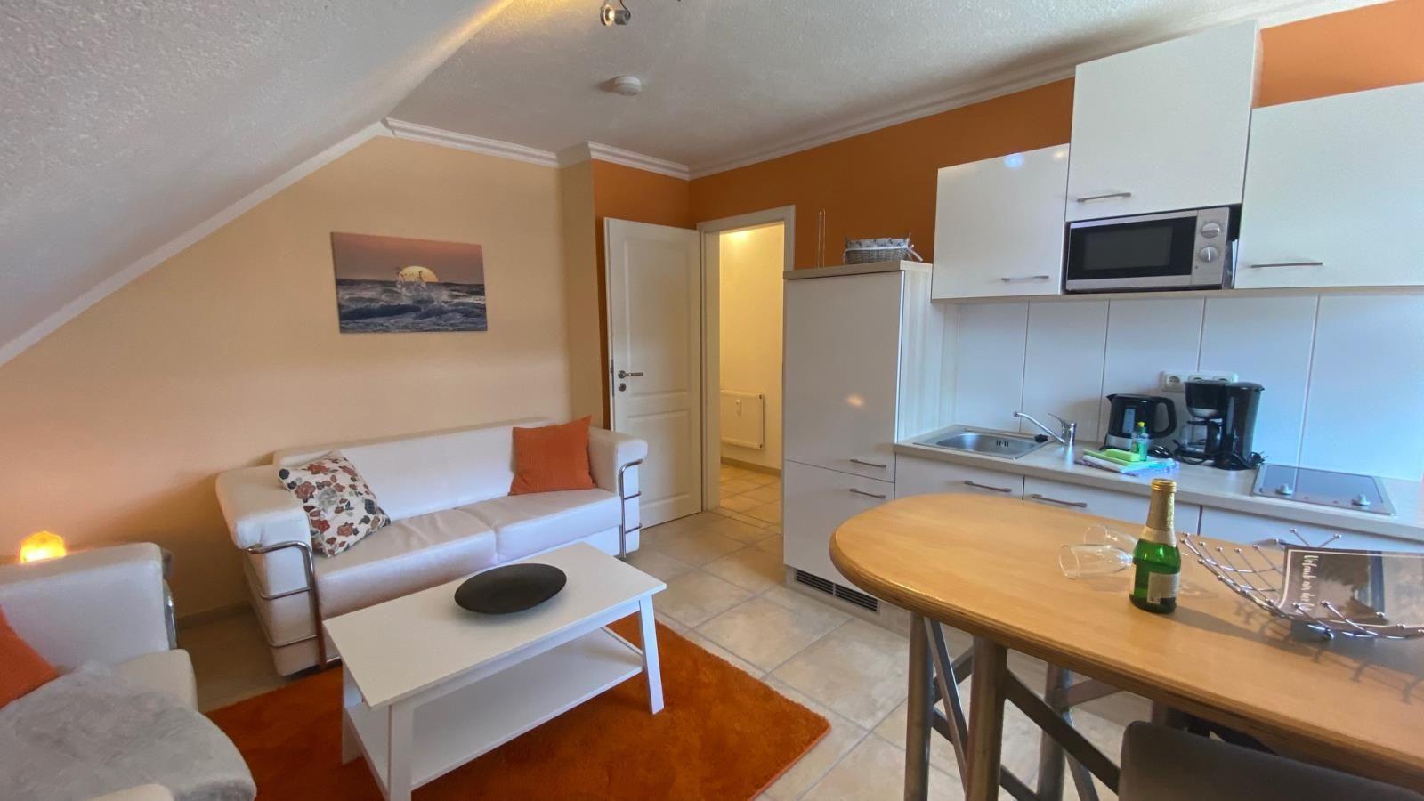 Wohnbereich mit Sofa, Couchtisch und Küchenzeile mit Mikrowelle und Kaffeemaschine.