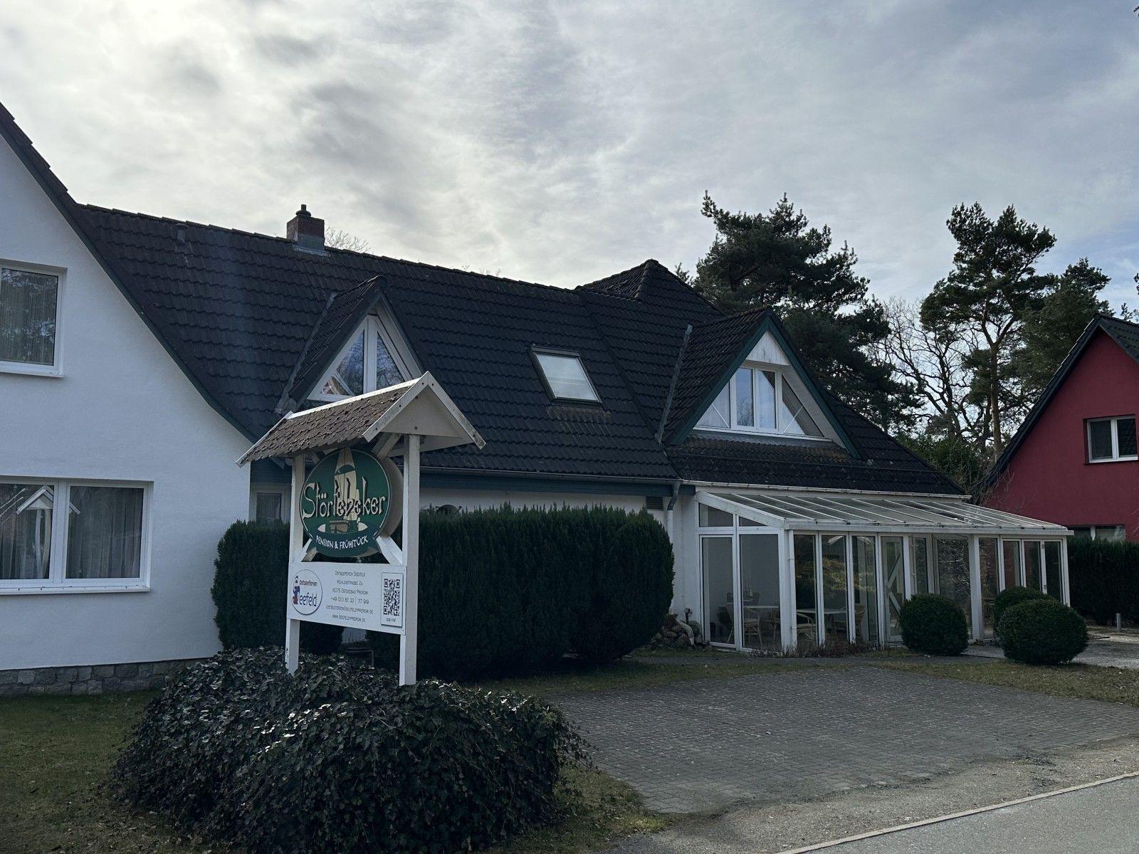 House with gabled roof, conservatory, and sign at entrance.