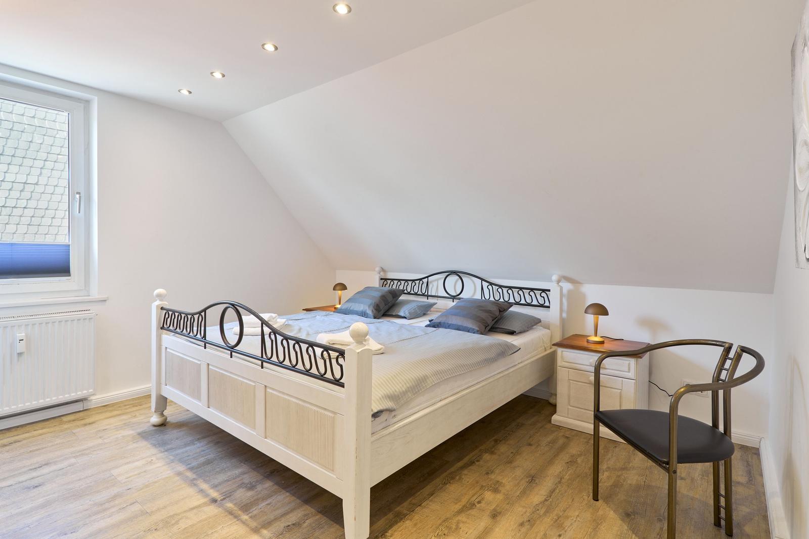 Schlafzimmer mit Dachschrägen, Bett, Nachttisch und Stuhl.