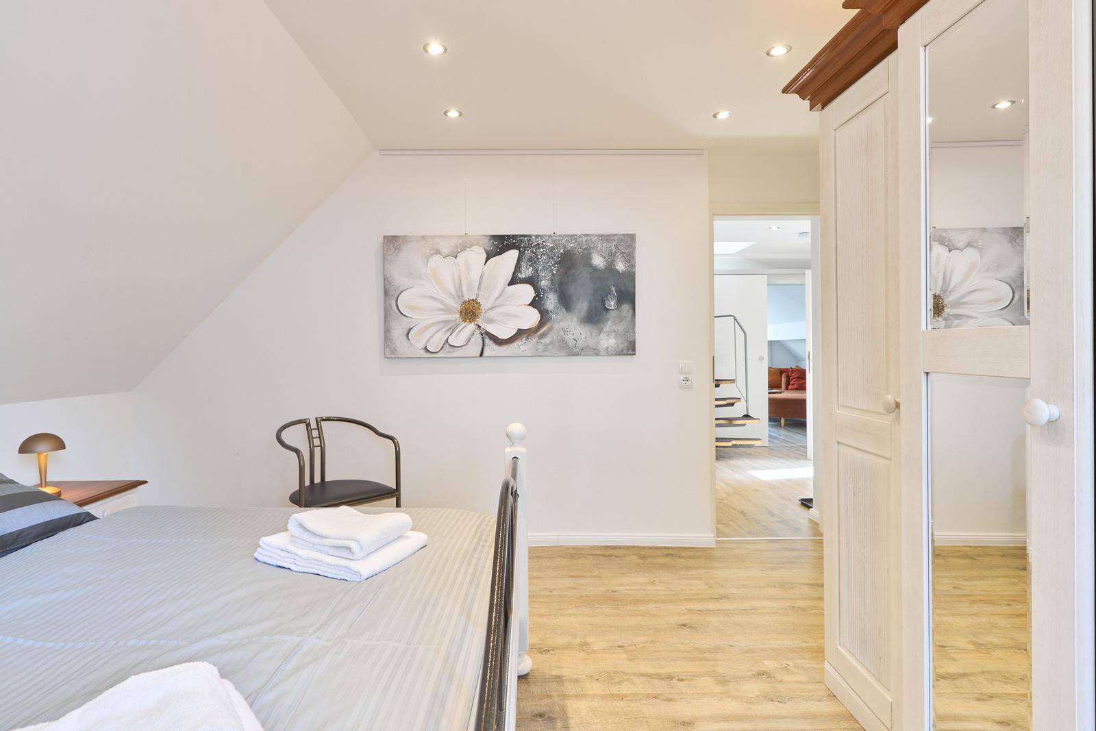 Schlafzimmer mit Bett, Wandbild und Blick in Wohnbereich.