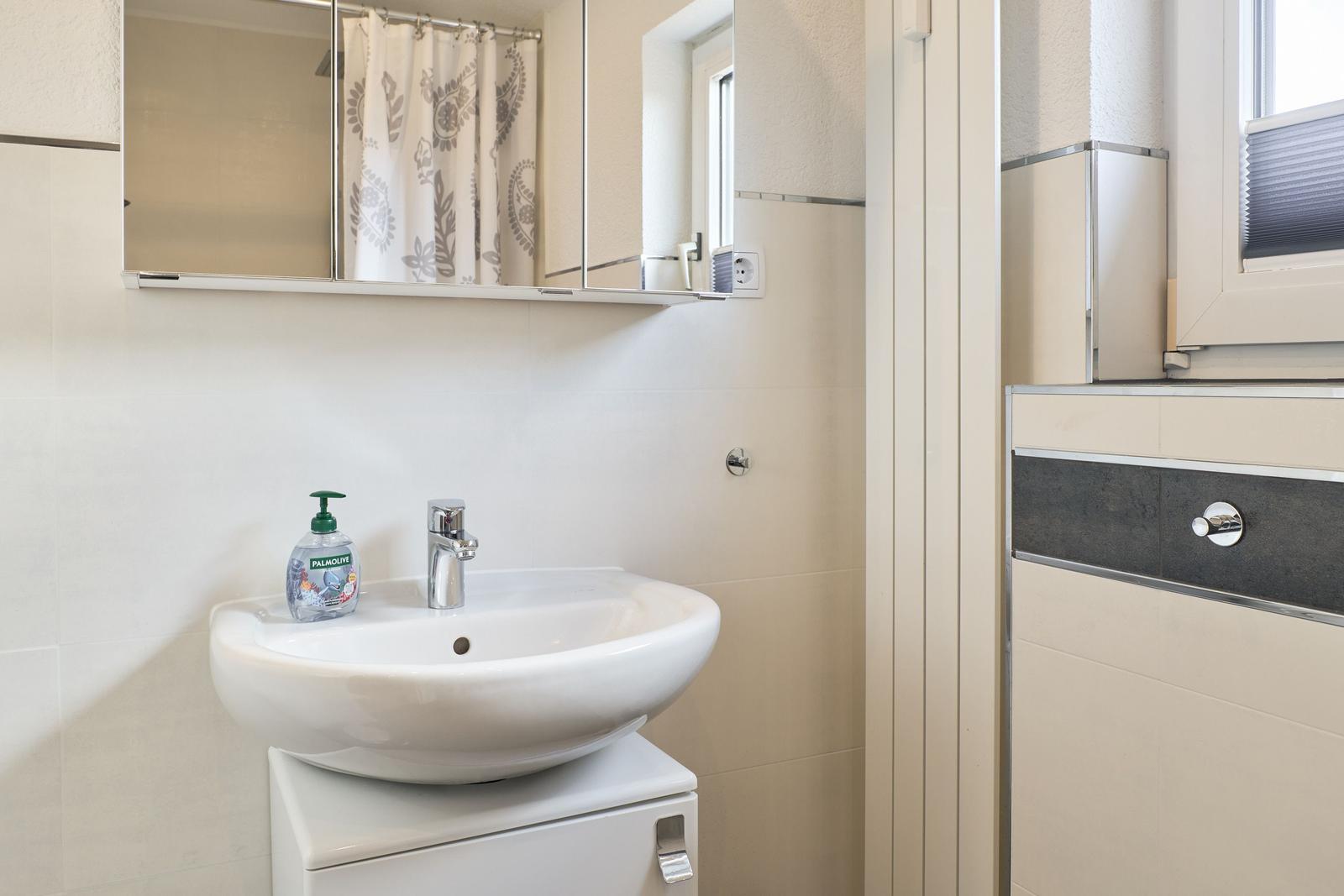 Badezimmer mit Waschbecken, Spiegel und Duschvorhang.