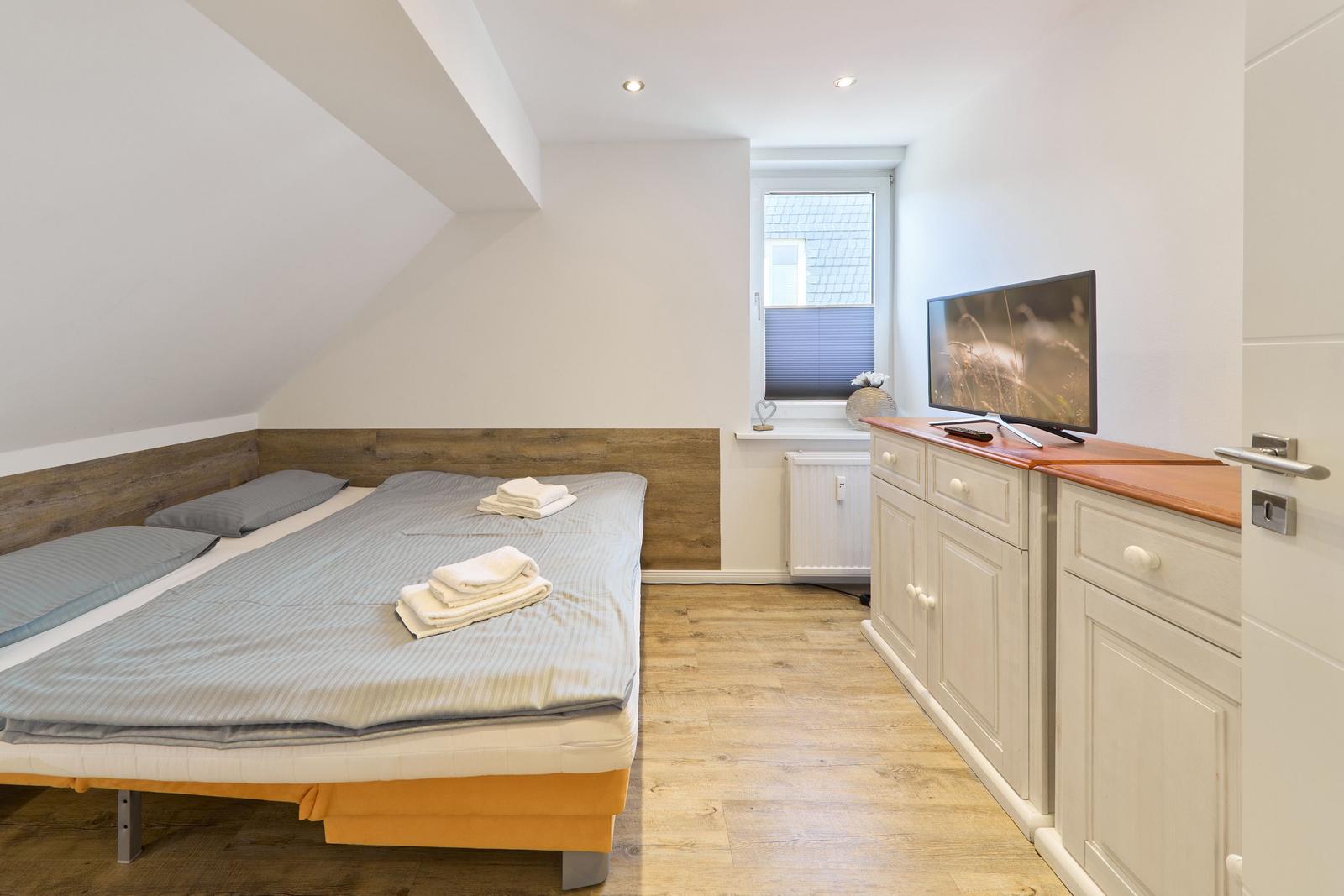 Schlafzimmer mit Doppelbett, TV und Fenster.