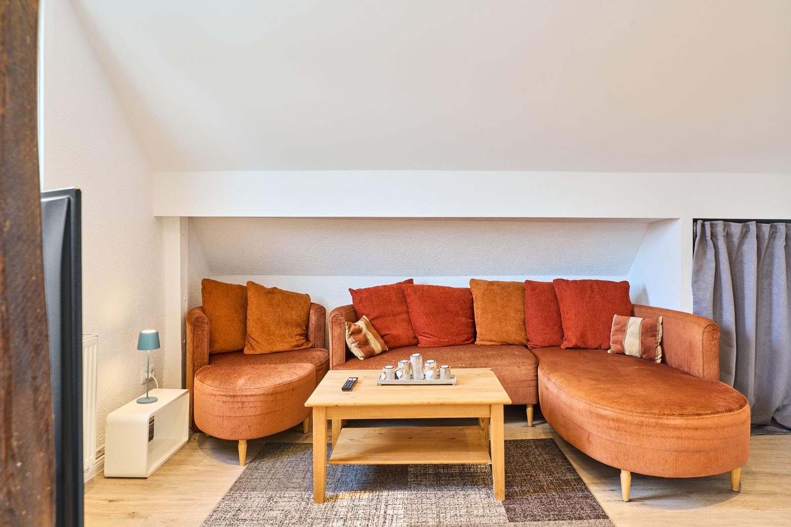 Ein Wohnzimmer mit orangefarbenem Sofa, Holztisch und Teppich.