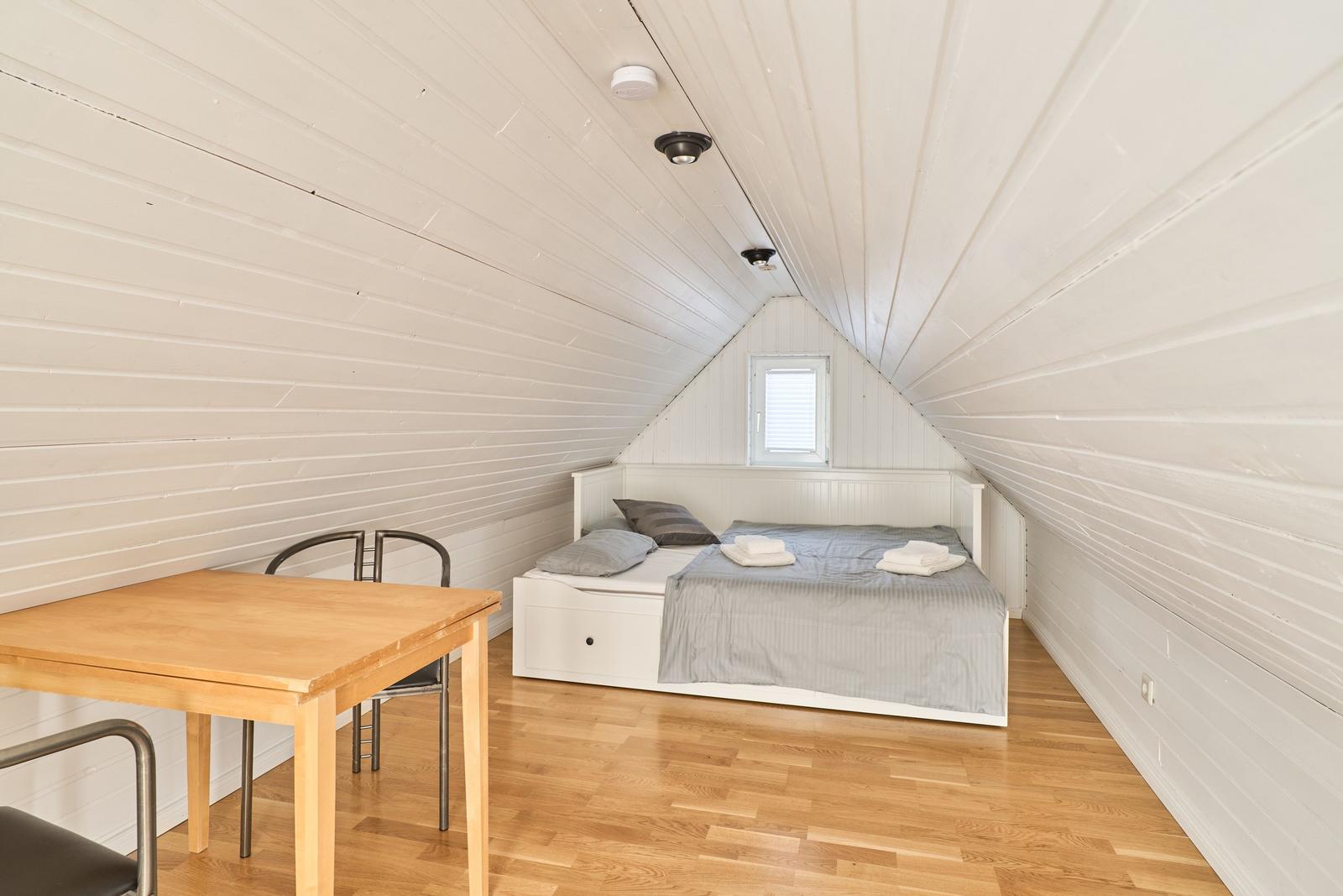 Zimmer mit Bett, Tisch und Stühlen unter schrägen Wänden.