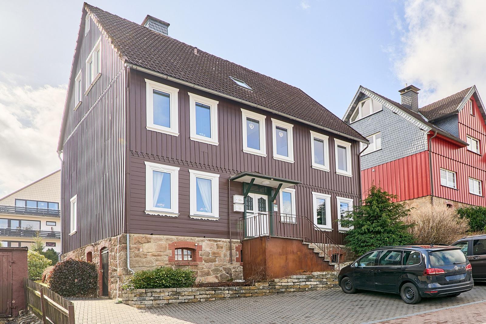 Haus mit braunem Holzschindeldach und Steinsockel. Vorhof mit gepflastertem Parkplatz.