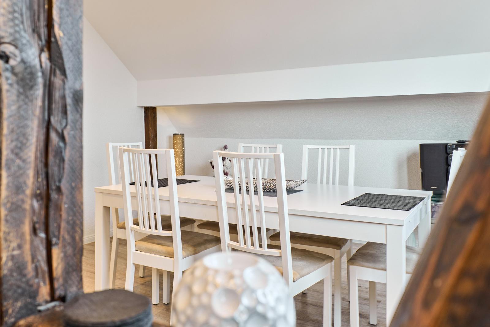 Esszimmer mit weißem Tisch und Stühlen, Holzwand und Deckenbalken