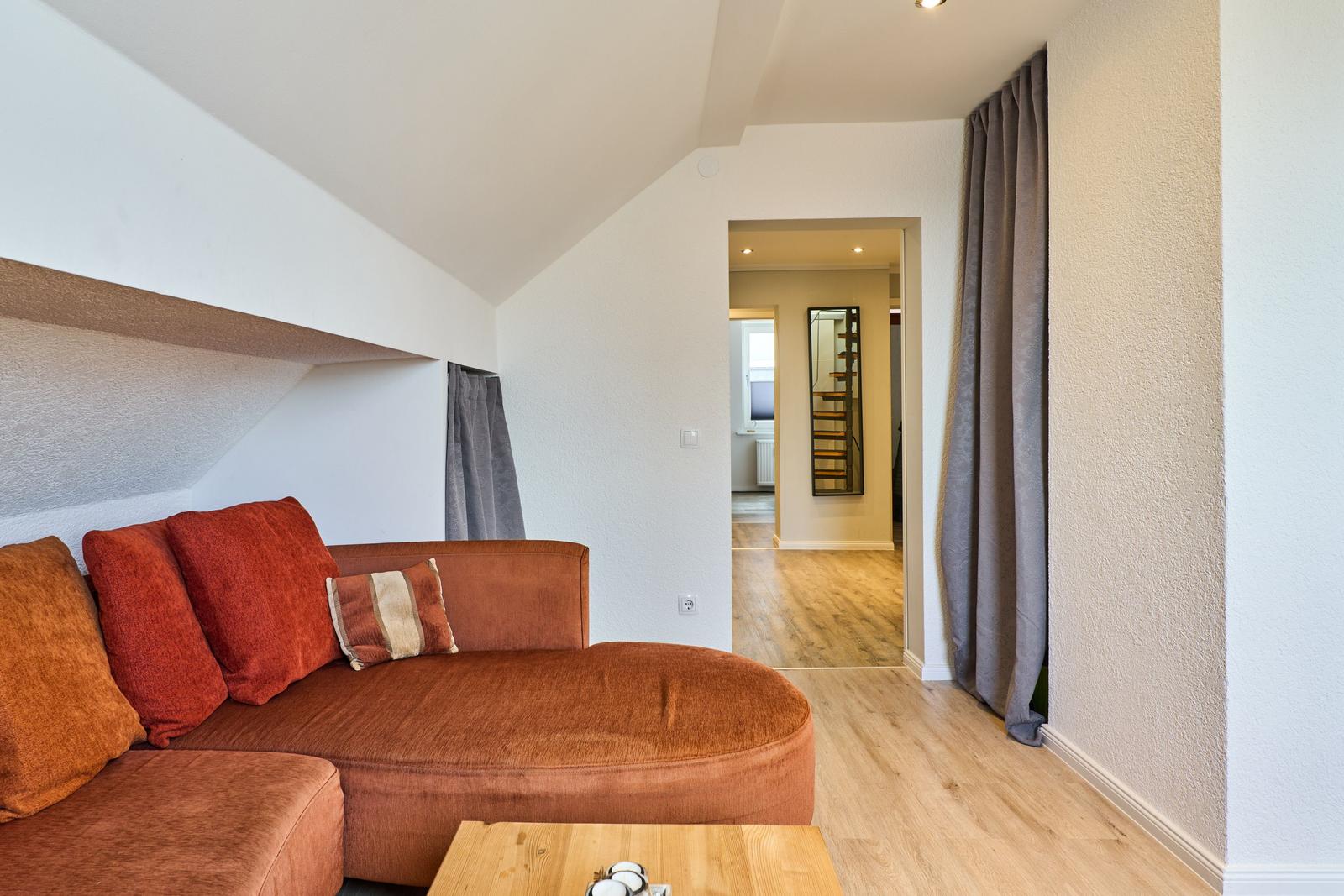 Wohnzimmer mit braunem Sofa, Holzboden und Blick in den Flur.