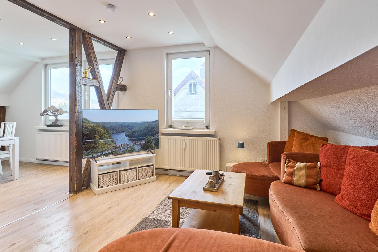 Wohnbereich mit Sofa, Fernseher und Holzboden unter Dachschrägen.