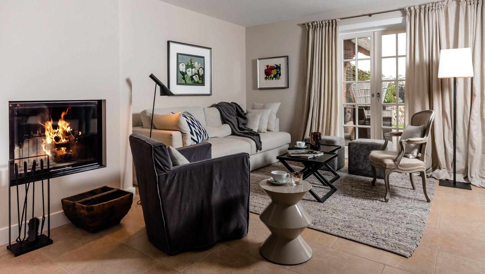 Wohnzimmer mit Kamin, Sofa, Sessel und Blick auf Balkon.