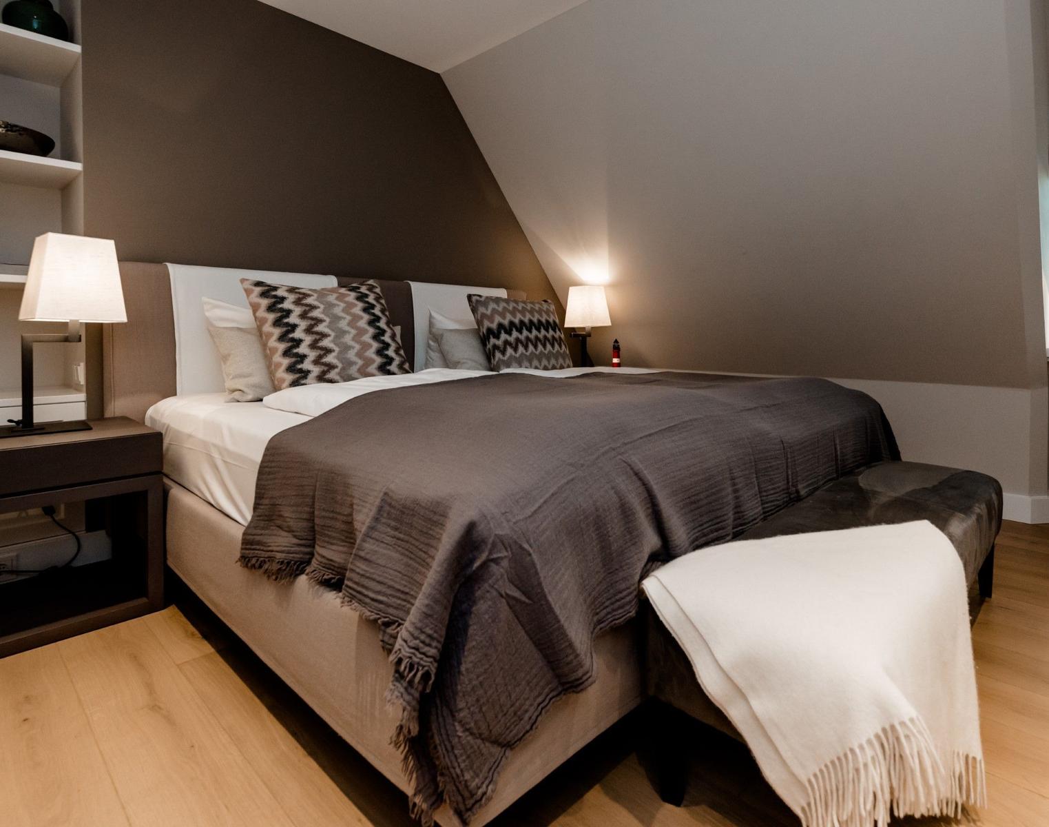 Schlafzimmer mit Dachschrägen, Bett mit Decke und Kissen, Nachttische mit Lampen.