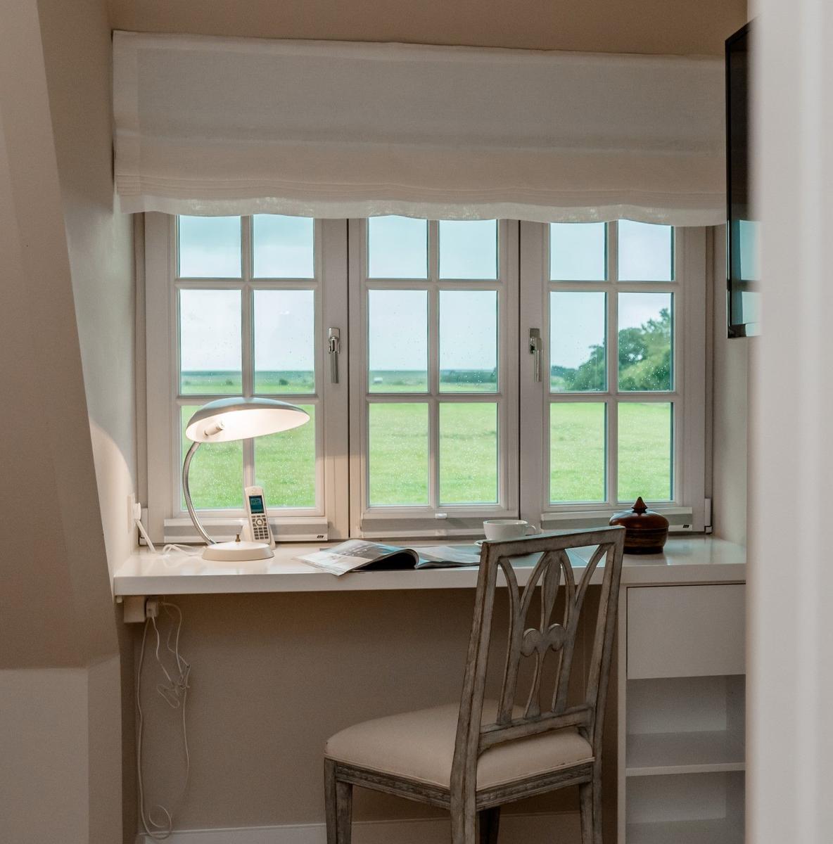 Schreibtisch mit Stuhl und Blick auf grünes Feld durch Fenster.