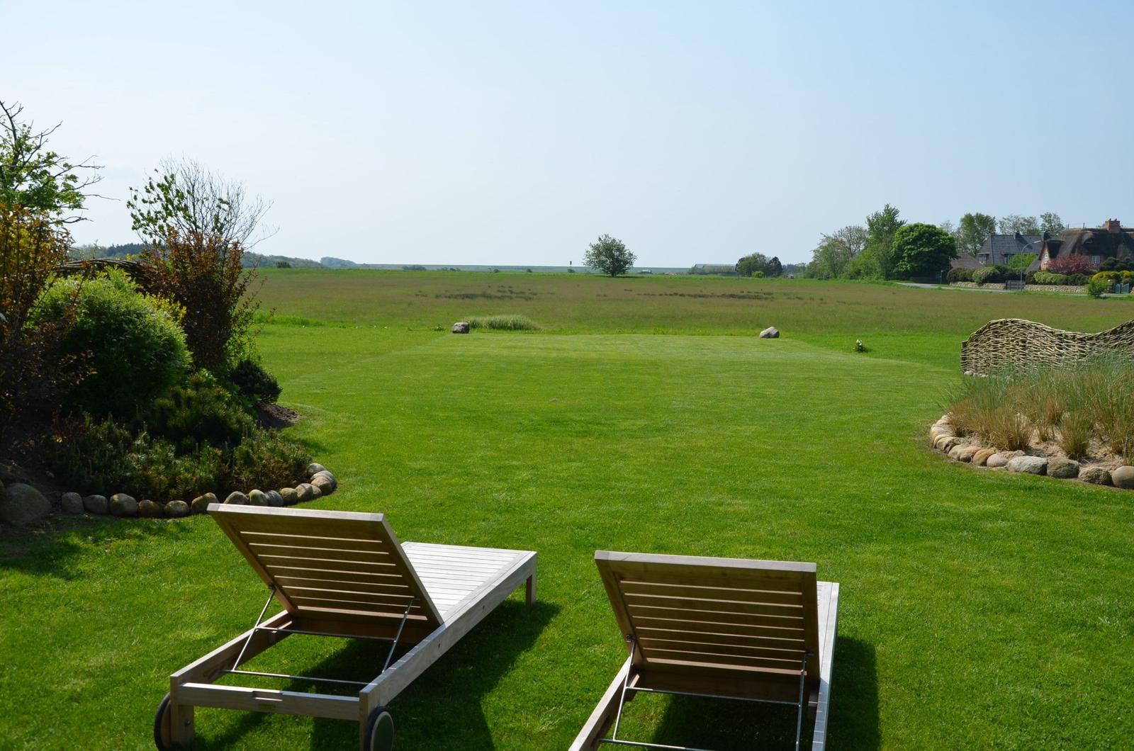 Zwei Liegestühle auf grünem Rasen mit Blick auf Feld und Himmel.