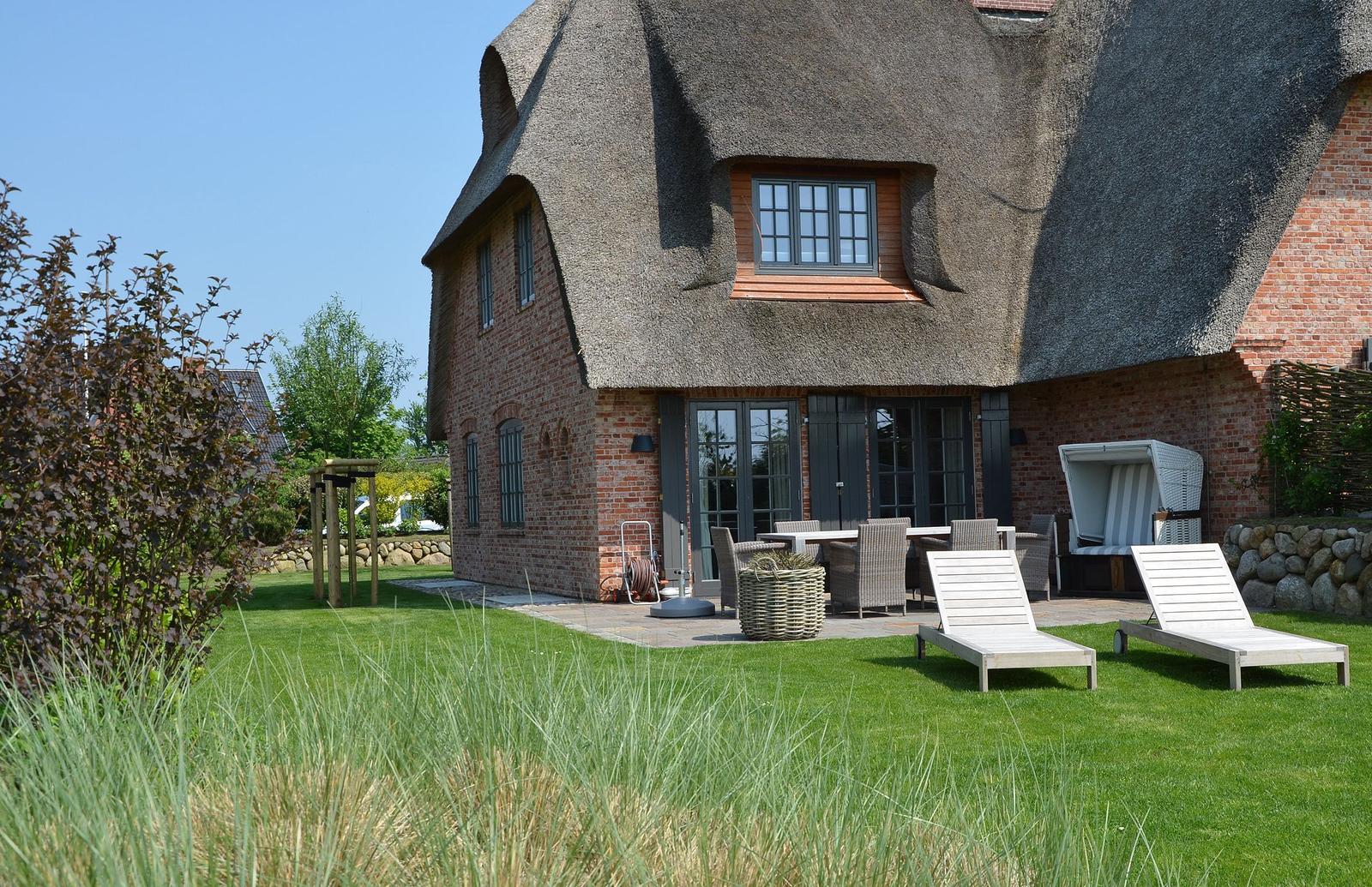 Haus mit Strohdach, Terrasse, Liegestühle und Garten.