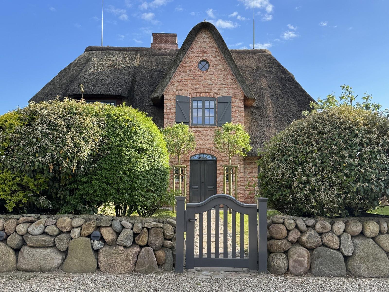 Rotes Backsteingebäude mit Strohdach, Eingangstor und Steinmauer.