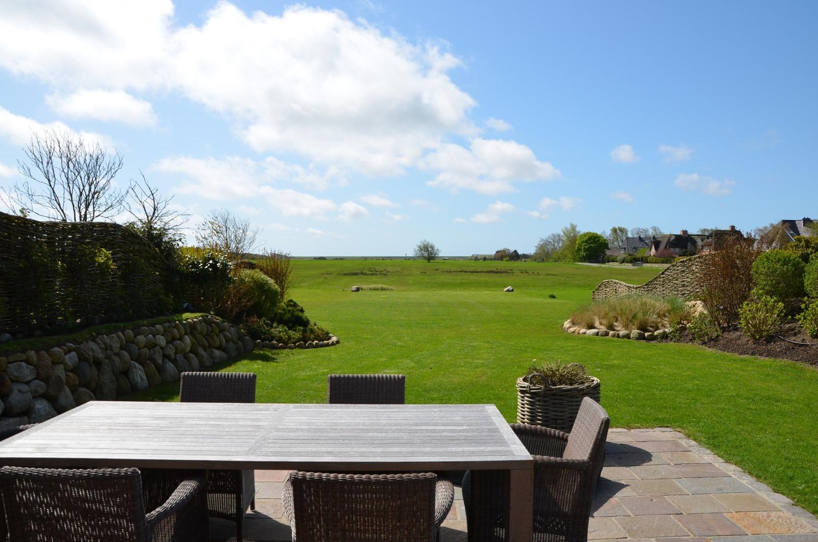 Terrasse mit Tisch und Stühlen, Blick auf grünes Feld und Himmel.