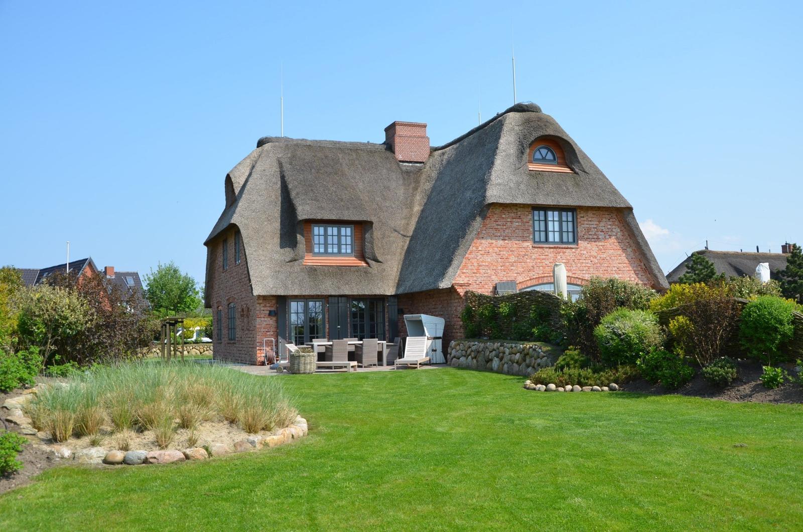Haus mit strohgedecktem Dach und großer Terrasse im Garten