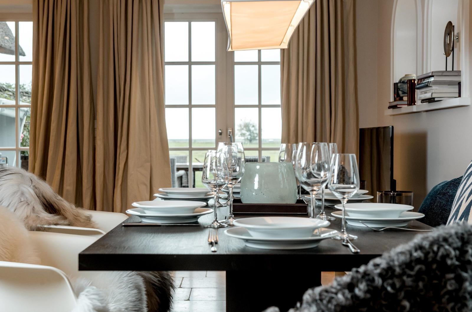 Esstisch mit Geschirr und Gläsern vor Fenster mit Blick auf Landschaft.