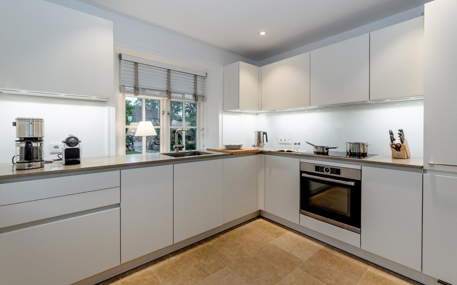 Moderne Küche mit weißen Schränken, Edelstahlgeräten und Blick auf Garten.