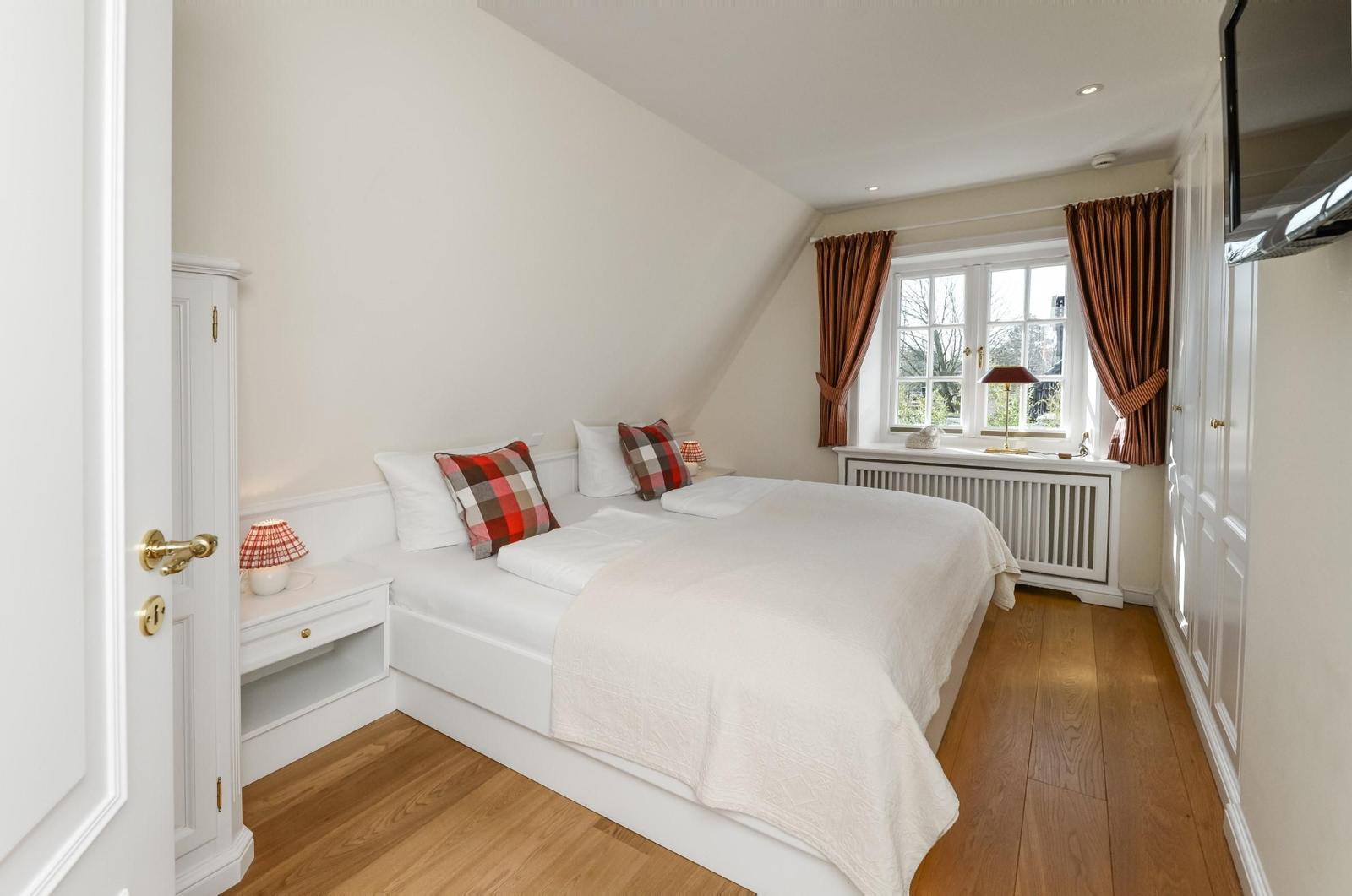 Schlafzimmer mit Dachschräge, Bett, Fenster und Holzboden.