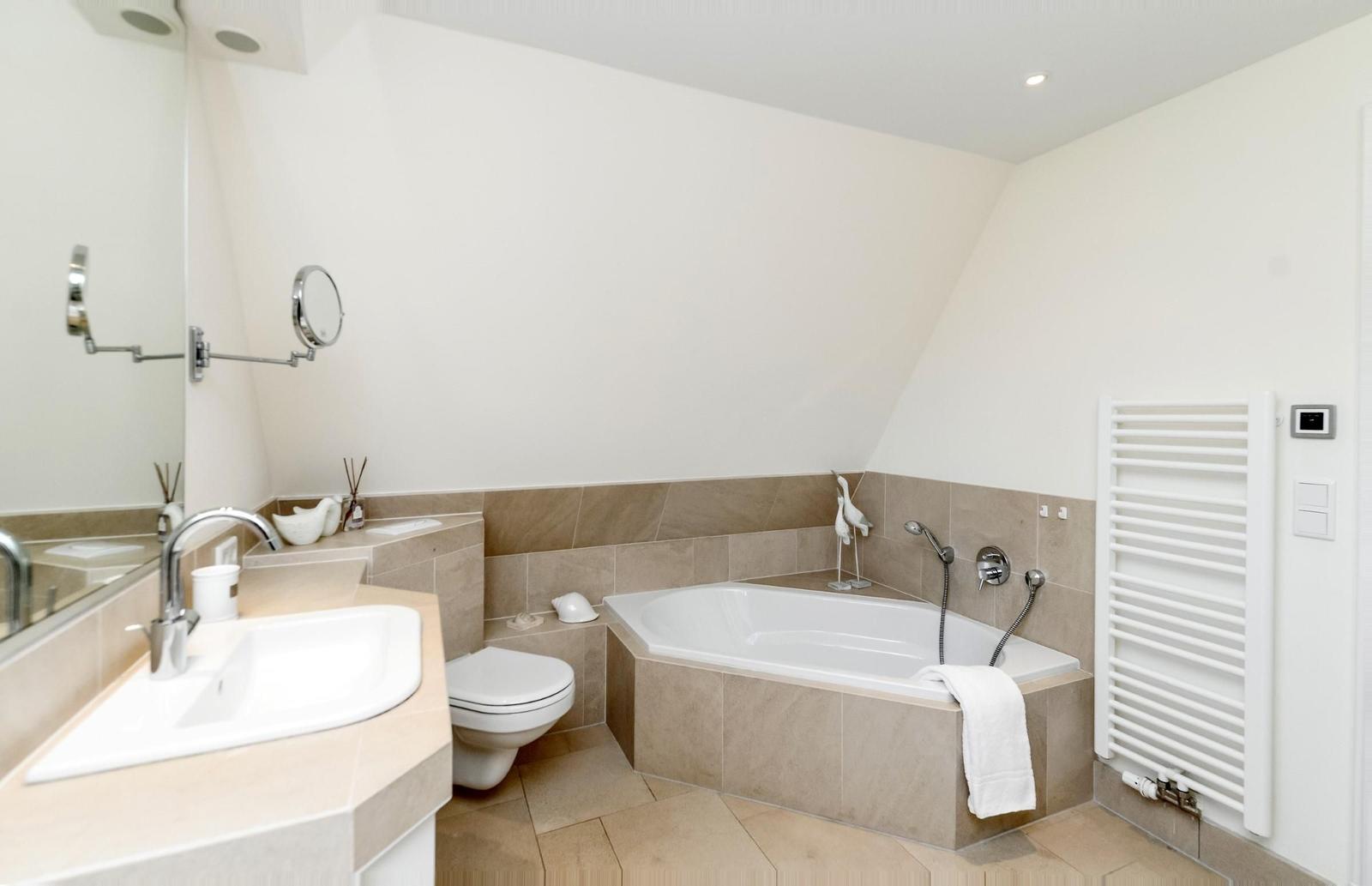 Badezimmer mit Badewanne, Waschbecken und Toilette. Weiße Wände und Fliesen.