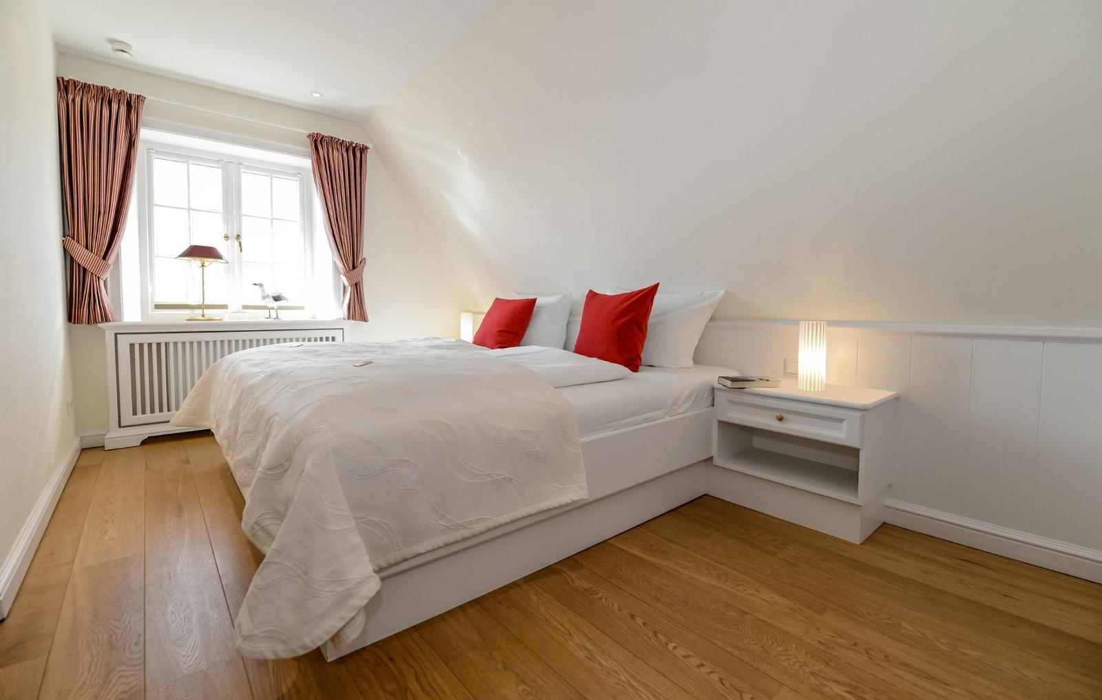 Schlafzimmer mit Bett, Nachttisch und Fenster mit Vorhängen.