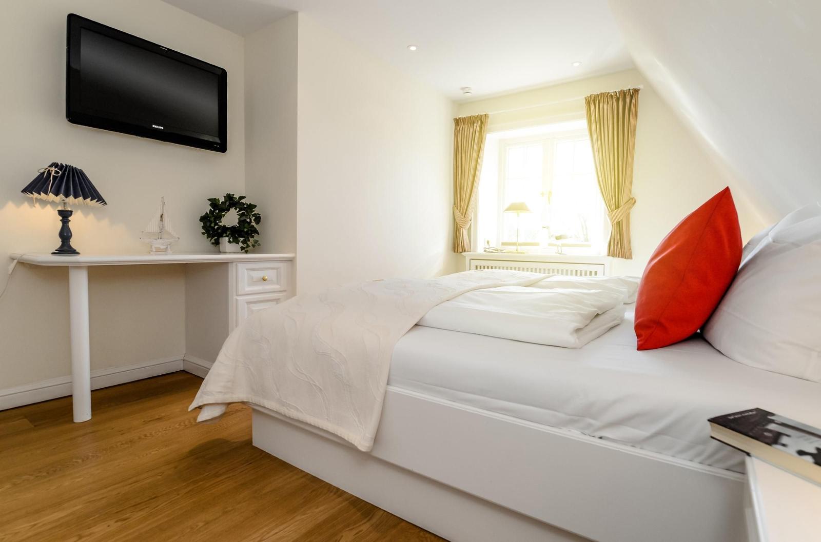 Schlafzimmer mit Bett, Fenster, TV und Schreibtisch.