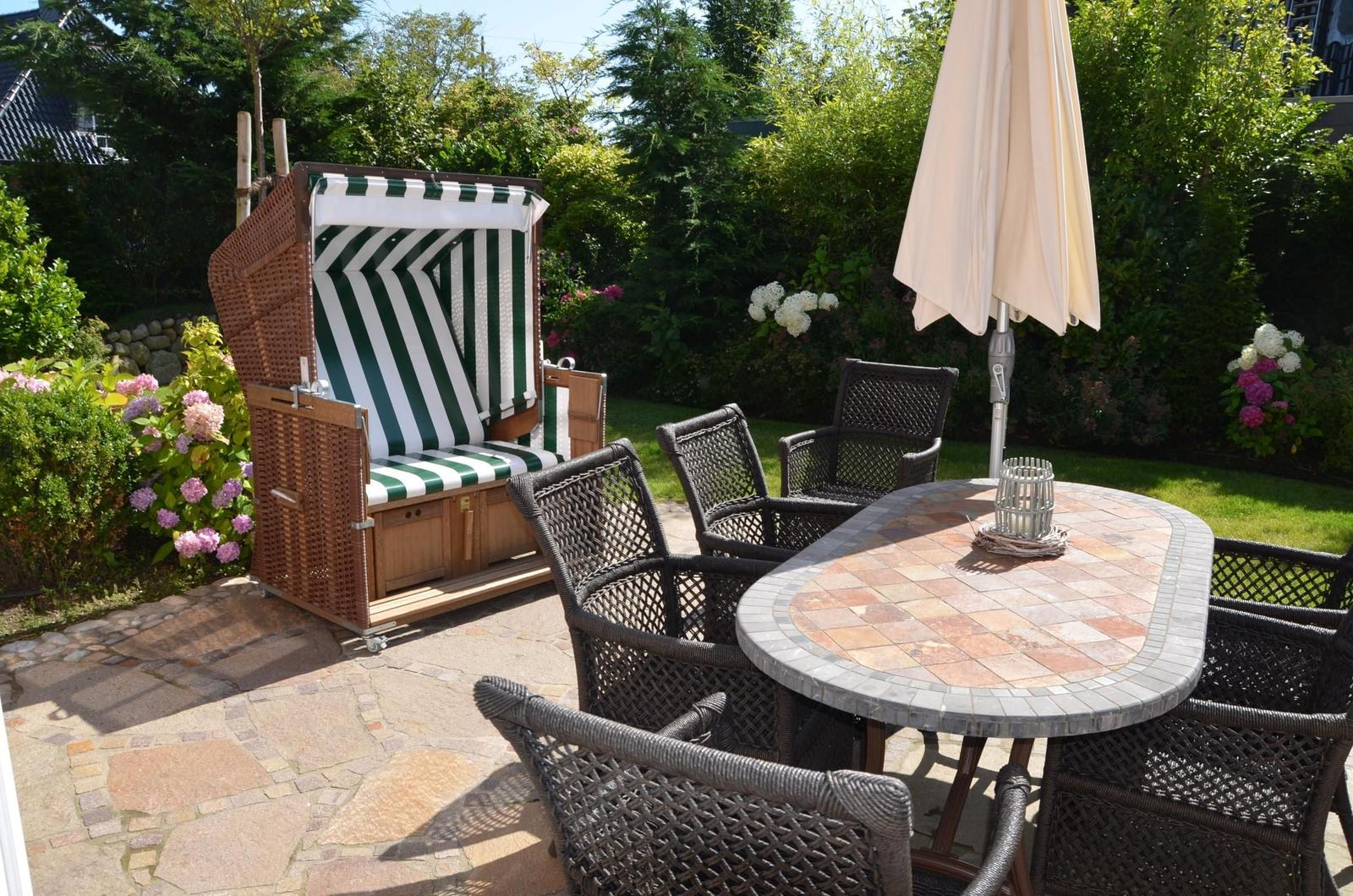 Garten mit Liegestuhl, Tisch und Stühlen, Sonnenschirm und Blumen.