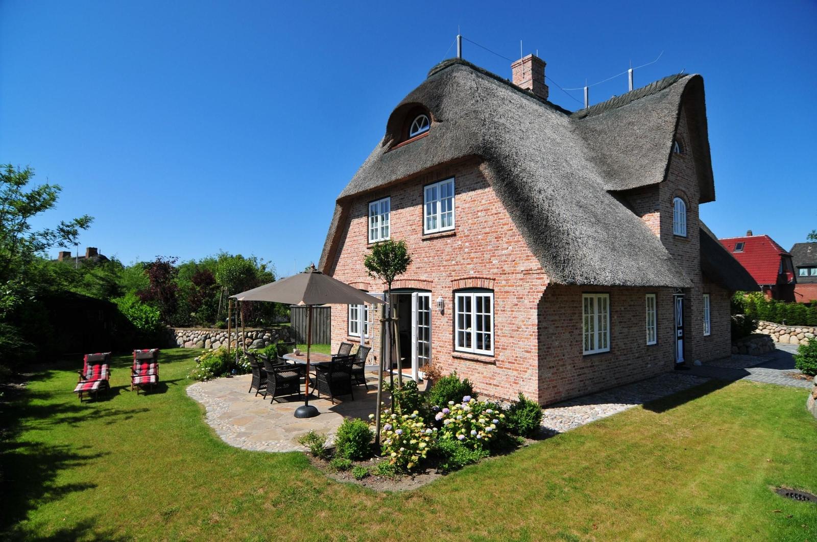 Rotes Backsteingebäude mit Strohdach, Garten mit Terrasse und Sitzgelegenheiten.