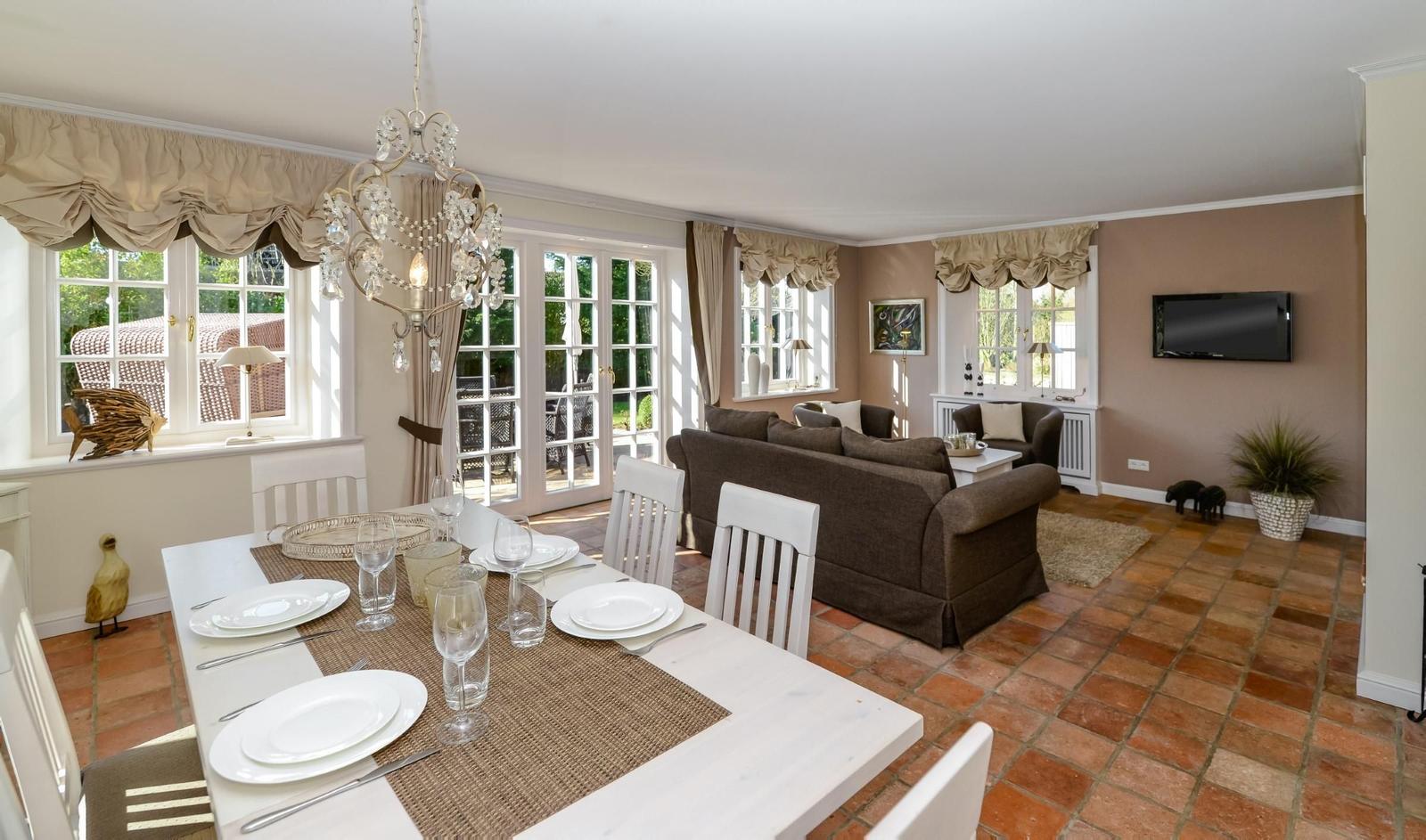 Esszimmer mit Esstisch und Sitzgelegenheiten. Durchgang zum Wohnzimmer mit Sofa und TV.