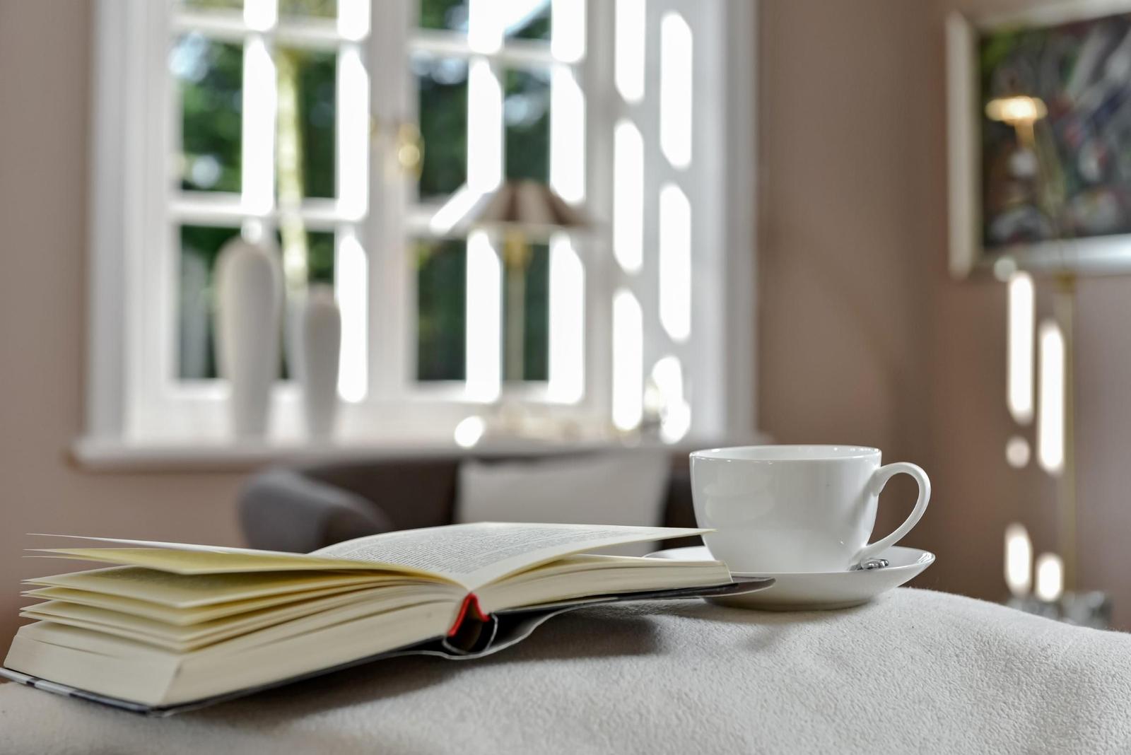 Ein Buch und eine Tasse stehen auf einem Tisch vor einem Fenster.