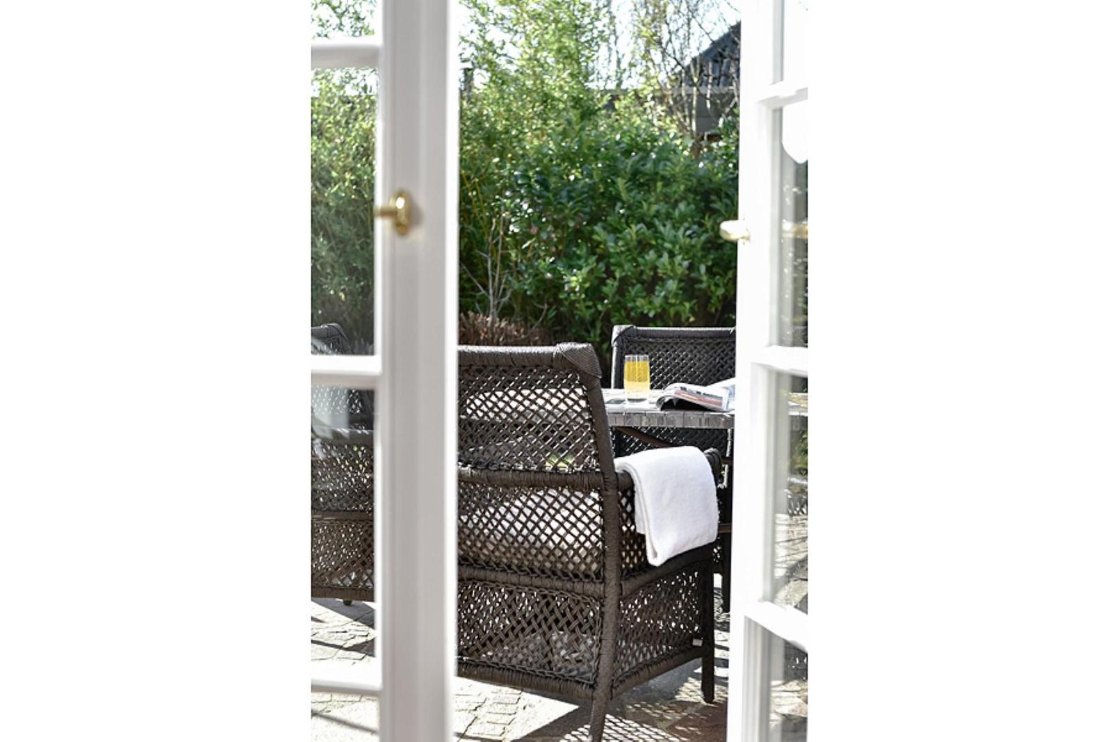 Durch offene Tür blickt man auf einen Außenbereich mit Rattanmöbeln und einem Tisch.
