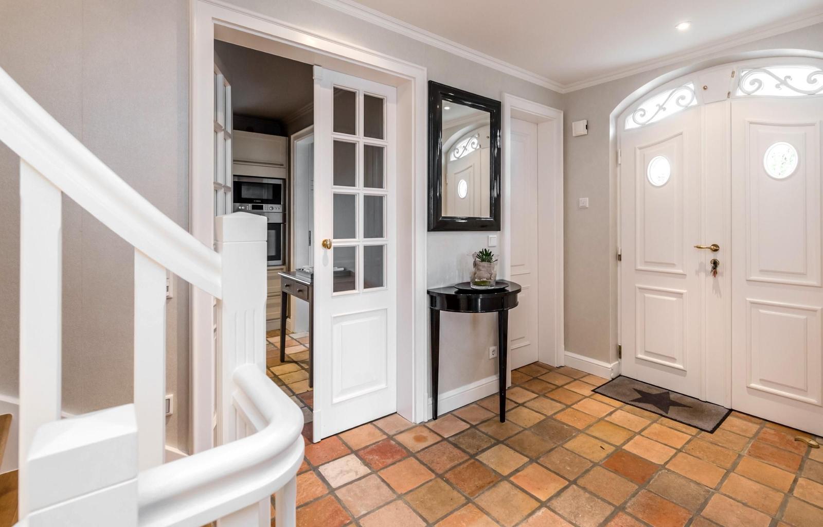 Eingang mit Terrakottboden, weißen Türen und Spiegel an der Wand.