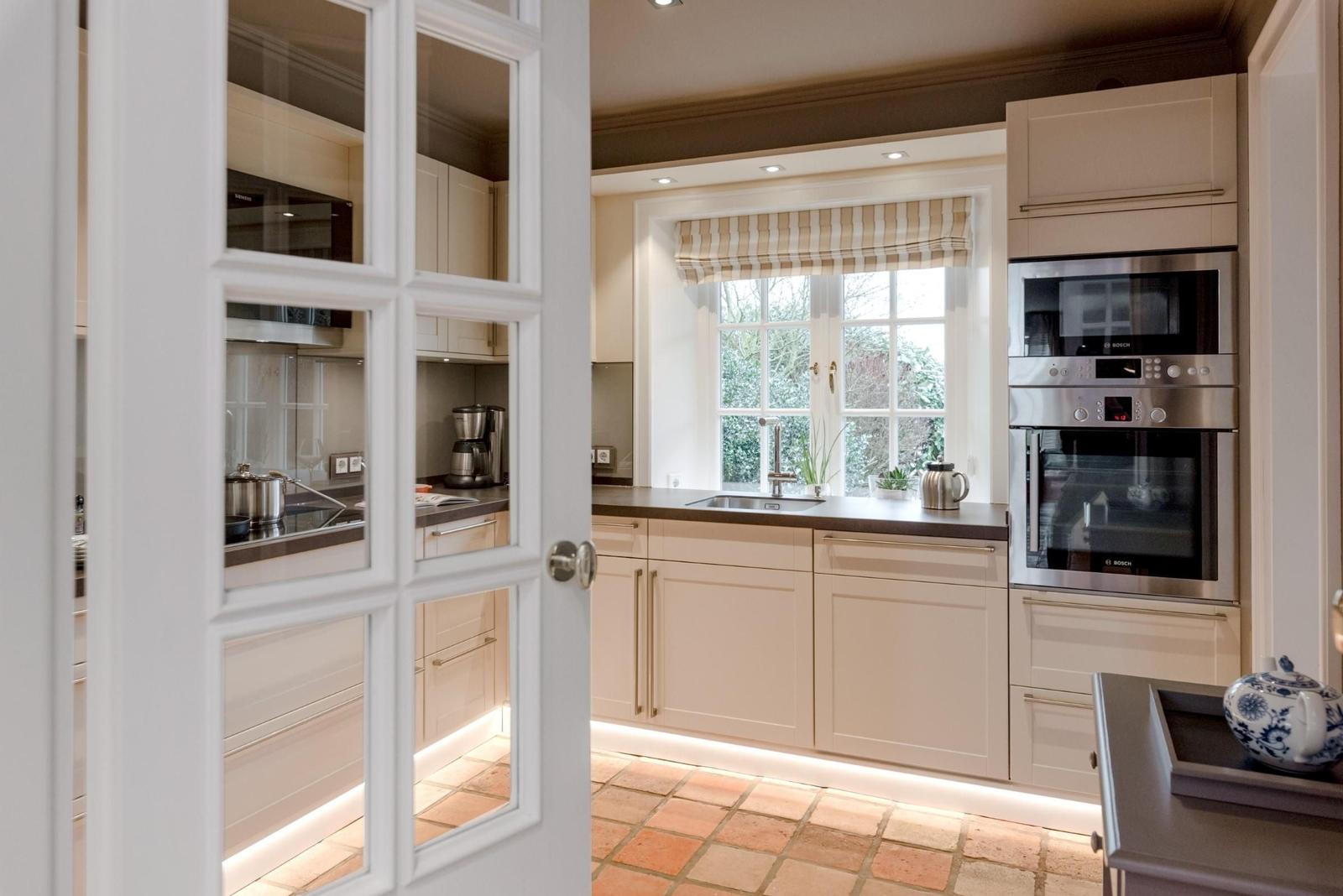 Küche mit weißen Schränken, Edelstahlgeräten und Terrakottaboden